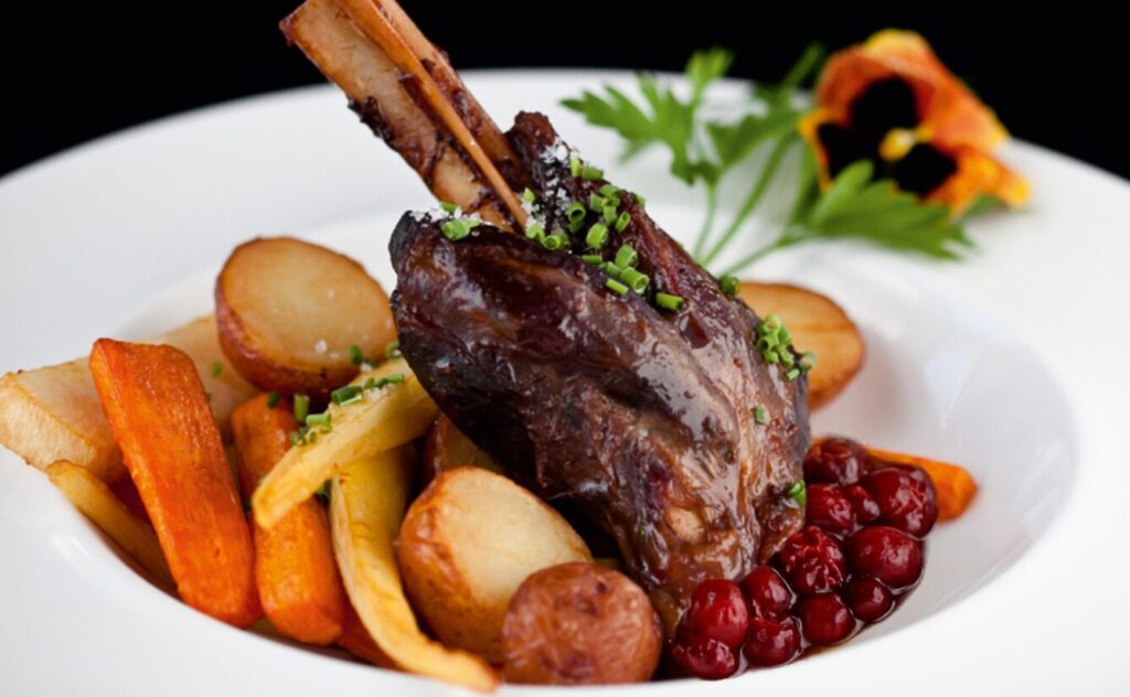 Jarret d’agneau braisé au sirop d’érable et aux canneberges, servi avec pommes de terre grelots et légumes racines rôtis.